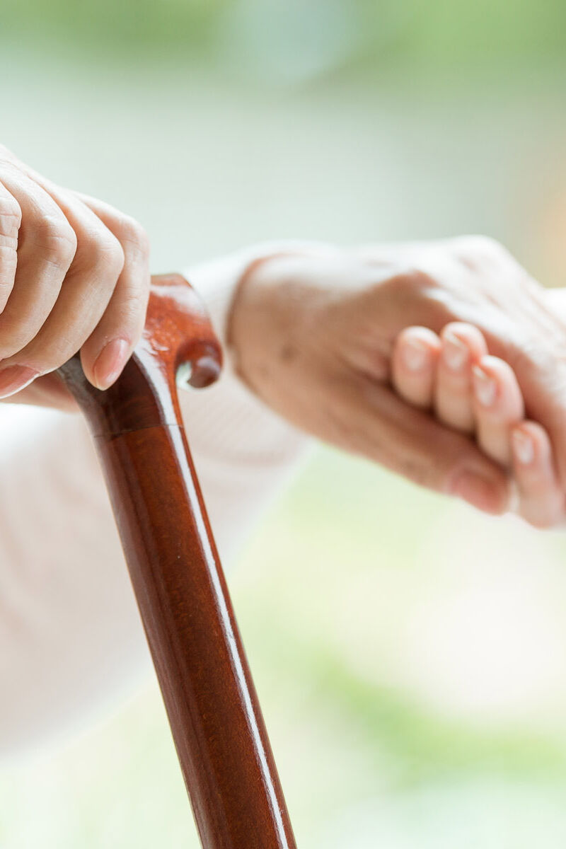 Closeup of elderly lady holding walking cane in one hand and holding volunteer's hand in the other