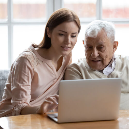 Grown-up daughter and old 80s father choose goods or services via internet or web surfing together at home. Younger generation caring about older relatives teaching using computer useful apps concept